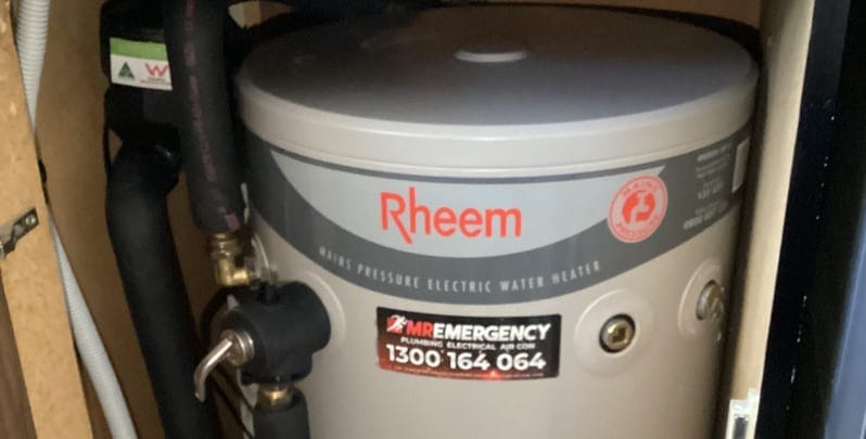 Top half of a Rheem electric hot water system. On it is a Mr Emergency sticker. 